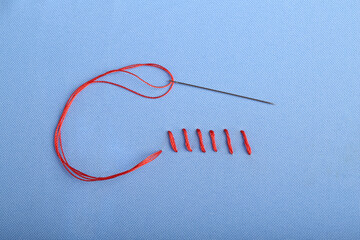 Sewing needle with thread and stitches on blue cloth, top view