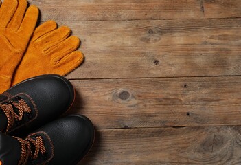 Pair of working boots and protective gloves on wooden surface, top view. Space for text