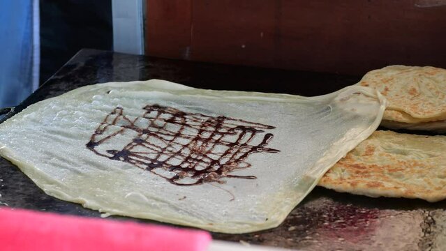 Street food vendor is preparing the dough and pan-frying paratha roti in hot oil until crispy on the outside. Street hawker preparing prata bread or roti canai for morning breakfast