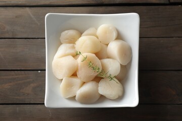 Fresh raw scallops and thyme in bowl on wooden table, top view