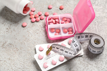 Container, bottle with weight loss pills and measuring tape on grey grunge background