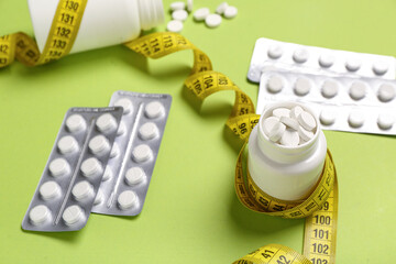 Bottle with weight loss pills, blister packs and measuring tape on green background