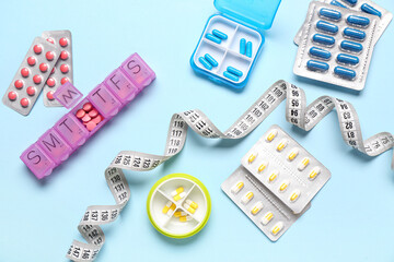 Containers, blister packs with weight loss pills and measuring tape on blue background