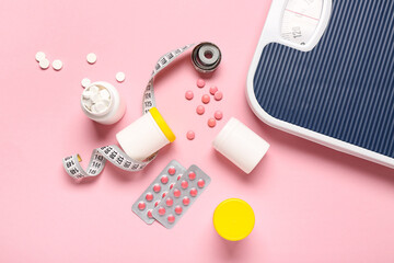 Bottles with weight loss pills, scales and measuring tape on pink background