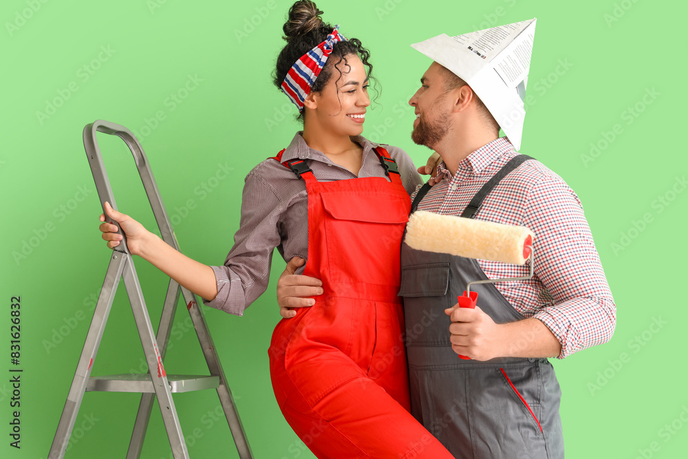 Wall mural Beautiful young happy couple with paint roller near green wall doing repair in new house