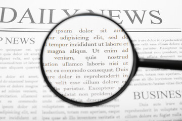 Daily newspaper with magnifying glass, closeup