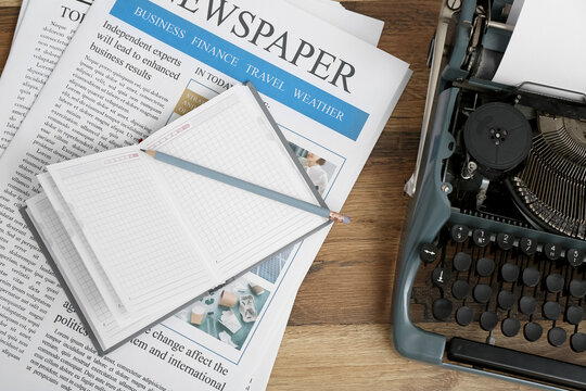 Newspapers with vintage typewriter and notebook on wooden background