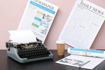 Obraz premium Newspapers with vintage typewriter and takeaway paper cup of coffee on black wooden table