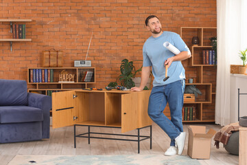 Young man with tools assembling chest of drawers at home