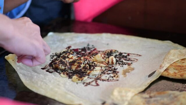 Street food vendor is preparing the dough and pan-frying paratha roti in hot oil until crispy on the outside. Street hawker preparing prata bread or roti canai for morning breakfast