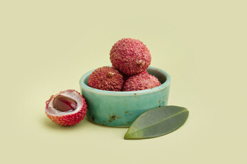 Bowl with tasty litchi fruit on green background