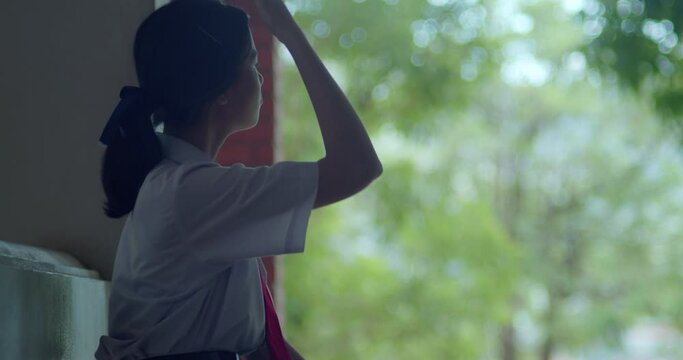 A silhouette scene of a young Asian high school girl with a highly private world or introvert, casually scrolling through social media on her smartphone in the evening after school.