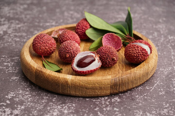Wooden plate with tasty litchi fruit on grunge background, closeup
