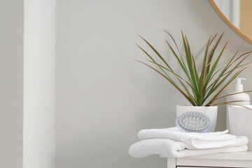 Towels with massage brush and plant on table in bathroom