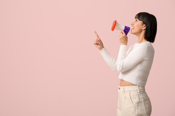 Young woman with megaphone pointing at something on pink background