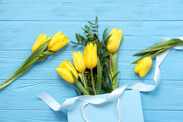 Paper shopping bag with yellow tulips on blue wooden background