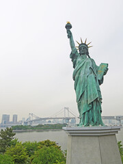 Fototapeta premium Statue of Liberty replica and Tokyo cityscape with famous Rainbow Bridge in background from Odaiba island waterfront