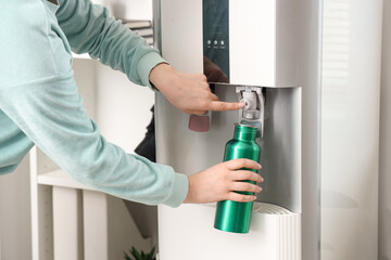 Female hands filling bottle with filtered water from cooler in room