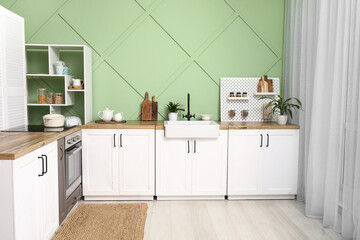 Interior of stylish kitchen with white counters, pegboard and green wall