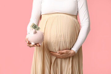 Pregnant young woman with piggy bank and money on pink background