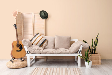 Interior of beige living room with cozy sofa, guitar, rug and houseplants