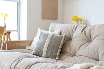 Interior of light living room with sofa, pillows and narcissus flowers