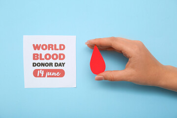 Female hand holding paper drop and paper sheet with text WORLD BLOOD DONOR DAY 14 JUNE on blue...