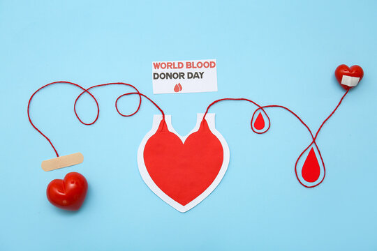 Composition with paper heart-shaped blood pack for transfusion, sheet with text WORLD BLOOD DONOR DAY, grip balls and paper drops on blue background - Powered by Adobe