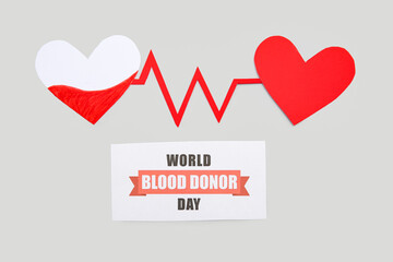 Paper sheet with sign WORLD BLOOD DONOR DAY and paper red hearts on grey background