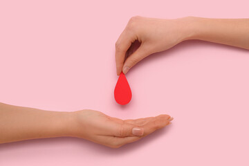 Female hands with red paper drop on red background. Donation blood concept.