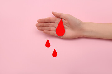 Female hand with paper blood drops on pink background. Donation blood concept.