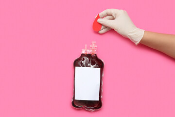 Female hand holding paper blood drop and blood pack for transfusion on pink background. World blood...