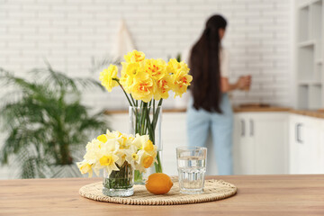 Beautiful bouquets of daffodils, glass of water and lemon on table at home, closeup