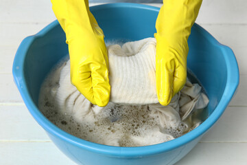 Woman in rubber gloves washing clothes in plastic basin on white table, closeup
