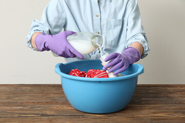 Woman in rubber gloves adding laundry detergent to clothes in plastic basin on wooden table against...