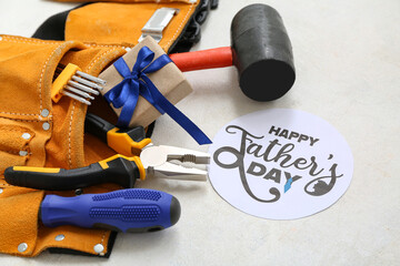 Tool belt with tools, gift box and greeting card with text HAPPY FATHER'S DAY on white grunge background