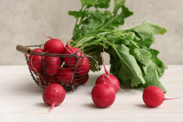 Basket with fresh radishes on white wooden table