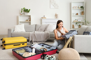 Female Asian traveler with organizer packing suitcase at home