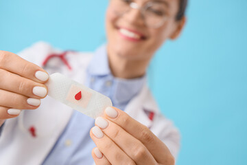 Female doctor with medical patch on blue background, closeup. Blood donation concept