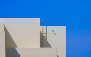 Geometric yellow office building with ladder on rooftop against blue clear sky background in minimal style, modern exterior architecture backdrop design