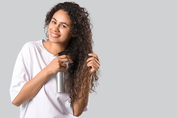 Beautiful young happy African-American woman with hair spray on grey background