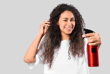 Beautiful young happy African-American woman with hair spray on grey background