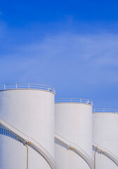 Three white storage fuel tanks in petroleum industry area against blue sky background in vertical...