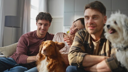 Pet owners relaxing couch watching tv together close up. Friends caressing dogs