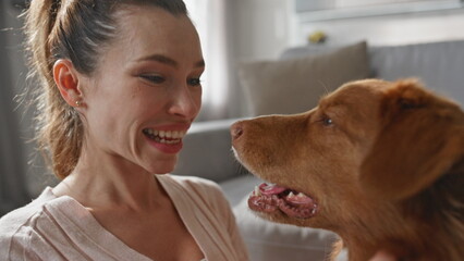 Closeup girl caressing dog muzzle in apartment. Smiling woman looking on pet 