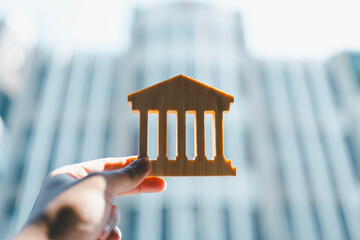 Business man holding bank symbol with blur white building. Concepts of the banking system, rising...