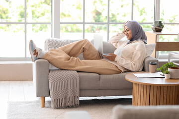 Muslim businesswoman with laptop lying on sofa at home