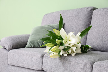 Bouquet of lily flowers on grey sofa in stylish living room, closeup