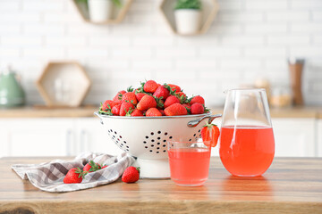 Colander with tasty strawberries and glass of juice on table in kitchen