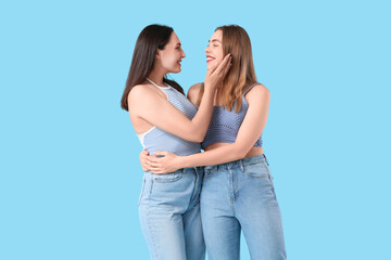 Beautiful young lesbian couple hugging on blue background